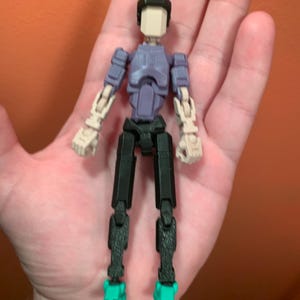 May include: A posable action figure with a purple torso, black legs, and teal shoes. The figure has a white head with a black helmet.