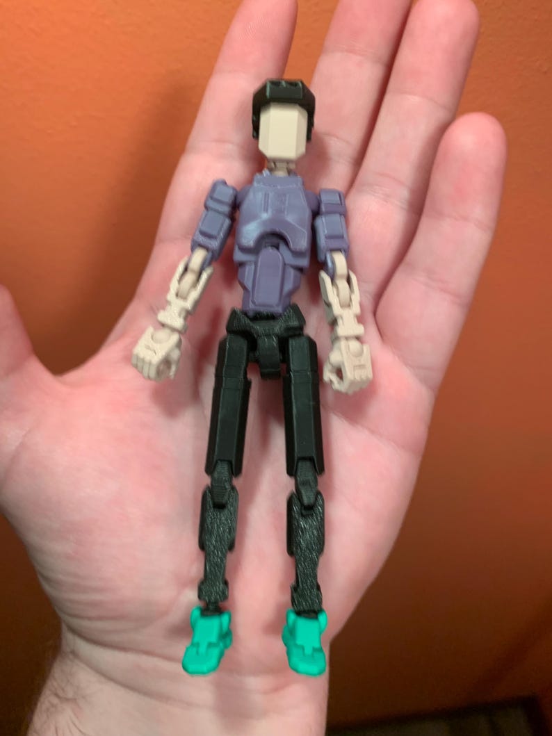 May include: A posable action figure with a purple torso, black legs, and teal shoes. The figure has a white head with a black helmet.