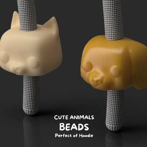 May include: Two animal-shaped beads, one cat and one dog, are displayed. The cat bead is a light beige color, and the dog bead is a golden yellow. Both are attached to a black and white patterned cord. The text "CUTE ANIMALS BEADS Perfect of Hoodie" is below.