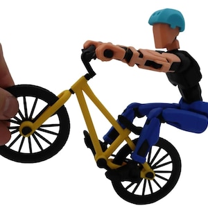 May include: A yellow and black BMX bike with a blue and black articulated figure riding it. The figure is wearing a blue helmet and is in a mid-air stunt pose.