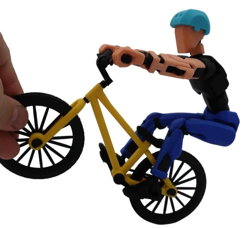 May include: A yellow and black BMX bike with a blue and black articulated figure riding it. The figure is wearing a blue helmet and is in a mid-air stunt pose.