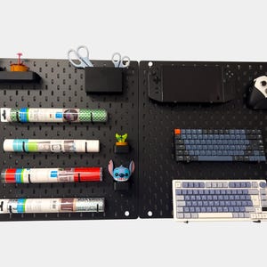 May include: Black pegboard wall organizer with various items, including rolls of wrapping paper, a small potted plant, a blue toy, scissors, a black storage bin, a keyboard, a gaming controller, and a tablet.