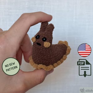 May include: A small brown crocheted sea slug plush with tan ruffled edges, two upright antennae, and black bead eyes. The image includes a green circle with the text NO SEW PATTERN, a US flag icon, a PDF download icon, and the text stitch.simple.