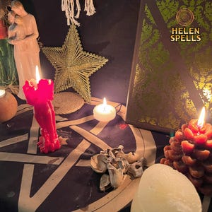 Op de afbeelding: Een rode kaars met een pentagram-ontwerp op een tafel met een wit tafelkleed. Er staan ​​andere kaarsen, een boek met de tekst "HELEN SPELLS" en gedroogde paddenstoelen op de tafel.