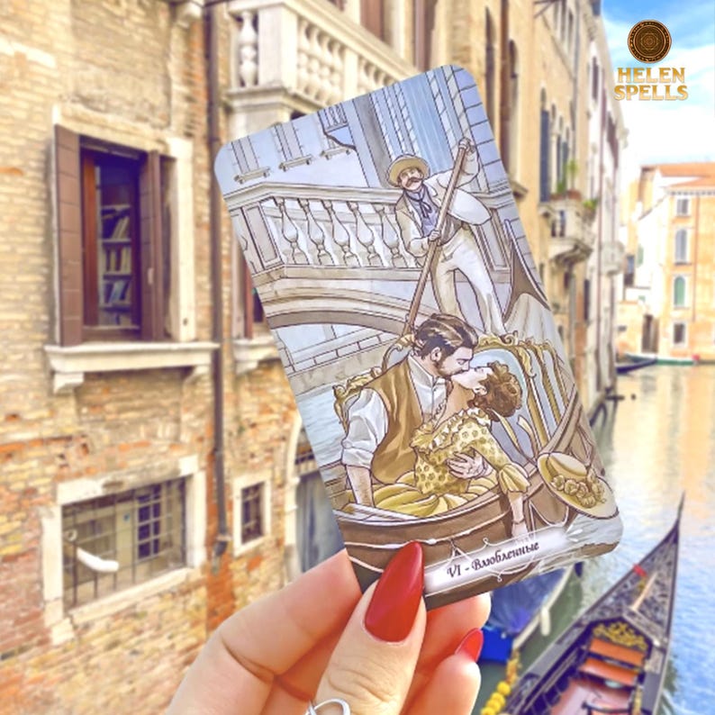 Puede incluir: Una carta del tarot que representa a una pareja bes&aacute;ndose en una g&oacute;ndola, con un gondolero en el fondo. La carta tiene una est&eacute;tica vintage, con una escena de canal y puente. La carta se sostiene frente a un fondo borroso de un canal y edificios.