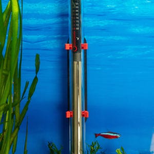 Könnte beinhalten: Ein zylindrischer Aquarienheizer aus Glas mit schwarzem Ober- und Unterteil, der eine vertikale Temperaturskala in Fahrenheit von 68 bis 93 Grad aufweist. Das Gerät ist mit zwei leuchtend orangefarbenen Clips vor einem blauen Hintergrund befestigt.