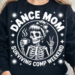 May include: Black sweatshirt with a white graphic. The graphic features a skeleton with a bun, holding a coffee cup and making a peace sign. Text reads "DANCE MOM SURVIVING COMP WEEKEND" in a circular design with star accents.