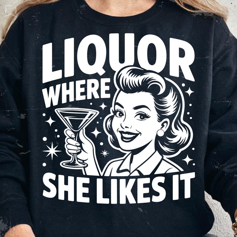 May include: Black sweatshirt with a white graphic. The graphic features a retro illustration of a woman holding a martini glass, with the text "LIQUOR WHERE SHE LIKES IT" in a bold, vintage font. The design includes star accents.