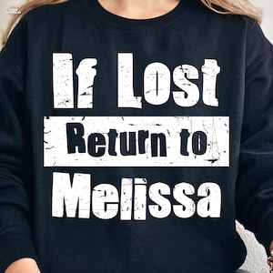 Könnte beinhalten: Schwarzes Sweatshirt mit dem Text "If Lost Return to Melissa" in verblichenen weißen Buchstaben. Der Text ist in drei Zeilen angeordnet, mit "Return to" in einem weißen Rechteck. Ein lässiges, bequemes Kleidungsstück.