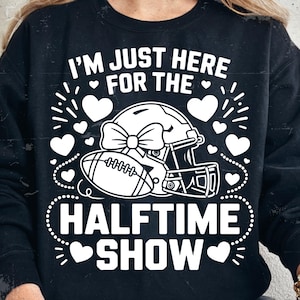 May include: Black sweatshirt with a white graphic that reads "I'M JUST HERE FOR THE HALFTIME SHOW." The graphic includes a football helmet with a bow, a football, and hearts.