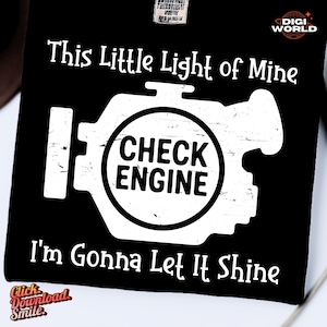 May include: Black graphic tee featuring a white engine design and the words "This Little Light of Mine, I'm Gonna Let It Shine." The design includes the words "CHECK ENGINE" in a circle.