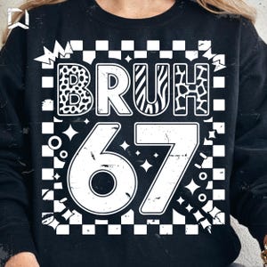 Puede incluir: Sudadera negra con un gráfico blanco. El gráfico incluye la palabra "BRUH" con letras con estampado animal y el número "67". El diseño está sobre un fondo a cuadros con acentos de estrellas y círculos.