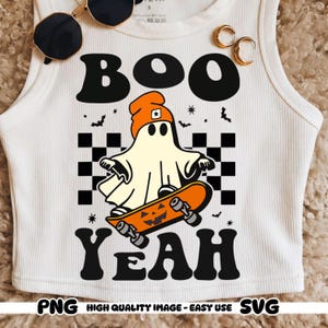 Può includere: Canotta bianca a coste con grafica a tema Halloween. Il design presenta un fantasma con un berretto arancione che cavalca uno skateboard arancione con una faccia di zucca. Le parole "BOO YEAH" sono sopra e sotto il fantasma.