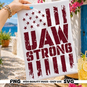 May include: White rectangular flag with a distressed burgundy design. The flag features a star field and stripes, with the words "UAW STRONG" in a bold, distressed font. The flag is held up by a hand with a bracelet.
