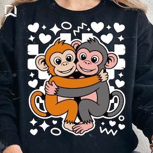 Peut inclure: Sweat-shirt noir avec un motif de deux singes de dessin animé qui s'embrassent. Un singe est orange, l'autre gris, sur un fond de coeurs blancs et de formes géométriques. Un design joyeux.