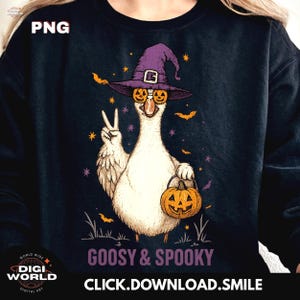 Peut inclure: Un sweat-shirt bleu marine avec une oie de dessin animé portant un chapeau de sorcière violet et des lunettes citrouille, tenant une lanterne citrouille. Le texte "GOOSY & SPOOKY" est en dessous de l'oie, avec des chauves-souris et des étoiles autour.