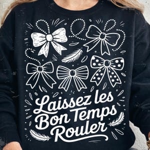Peut inclure: Sweat-shirt noir avec un motif graphique blanc représentant plusieurs nœuds et l'expression « Laissez les Bon Temps Rouler ». Les nœuds présentent divers motifs, dont des pois. Des plumes et des lignes pointillées complètent le design.