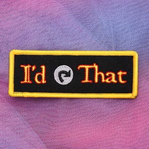 Könnte beinhalten: Ein rechteckiger, schwarzer Aufnäher mit gelbem Rand und dem roten Schriftzug "I'd That", sowie einem weißen und grauen gebogenen Pfeilsymbol. Der Aufnäher befindet sich auf einem farbenfrohen, verlaufenden Hintergrund.