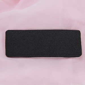May include: A rectangular black fabric patch with rounded corners. The patch has a textured surface and is set against a soft, light pink background. The fabric appears to be tightly woven.