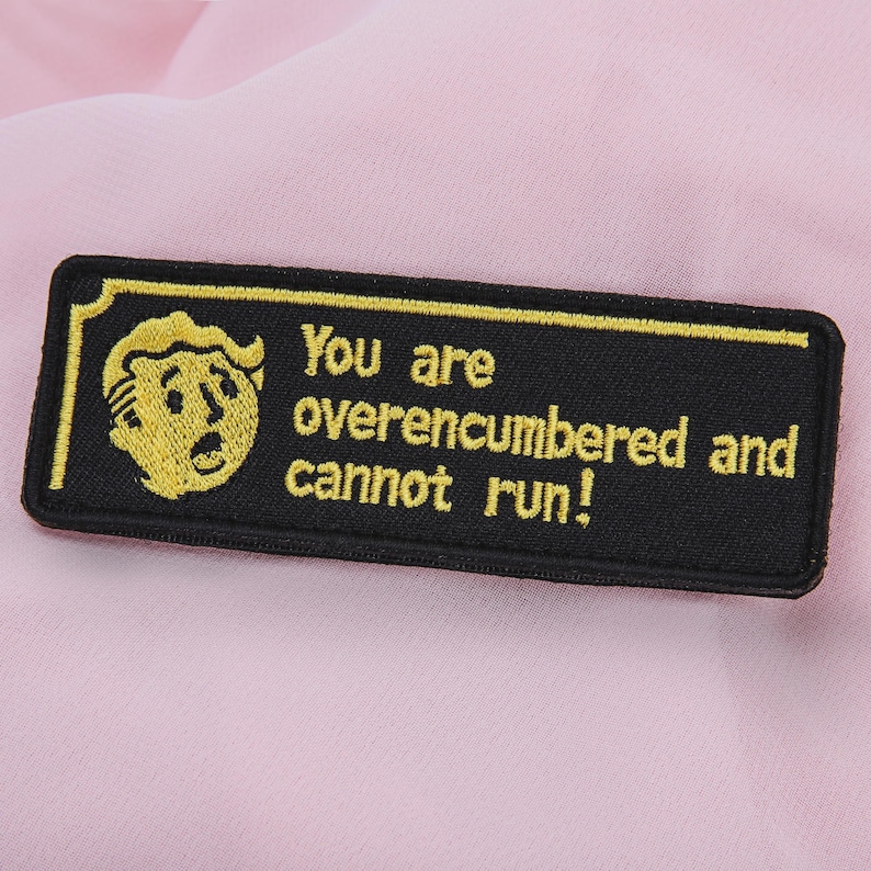 May include: Black rectangular patch with a yellow border and a yellow cartoon character on the left. The text "You are overencumbered and cannot run!" is embroidered in yellow.
