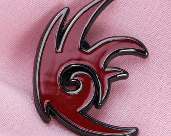 Può includere: Spilla in smalto rosso e nero con un design a fiamma stilizzato. La spilla presenta un centro rosso lucido con un contorno nero, creando un contrasto sorprendente. Il design include linee curve e un elemento a spirale, suggerendo un tema dinamico.