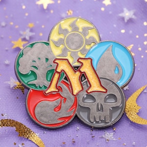 May include: A silver metal pin with a stylized "M" in the center surrounded by five colored circles. The circles represent the five colors of magic in the game Magic: The Gathering: white, blue, black, red, and green.