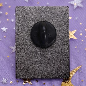 May include: The back of a black enamel pin with a black rubber clutch back.