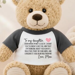 May include: A tan plush teddy bear wearing a white and dark gray raglan shirt. The shirt features black text that reads: To my daughter, Even when I'm not close by, I want you to know I love you, and that I'm thinking about you always. Love, Mom.