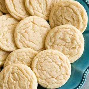 May include: A close-up shot of several golden-brown sugar cookies arranged on a teal, scalloped-edge plate. The cookies have a crinkled surface and a soft, inviting appearance, perfect for a sweet treat.