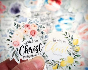 May include: Two die-cut vinyl stickers featuring floral designs and the text "Rejoice in Christ Philippians 4:4". One sticker displays pink and white roses with eucalyptus, while the other shows yellow lemons and green leaves.