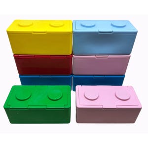 May include: A collection of six rectangular storage boxes arranged in two columns. The boxes are colored yellow, red, blue, light blue, pink, and green. Each box features a hinged lid with two circular studs on top, resembling large building blocks.
