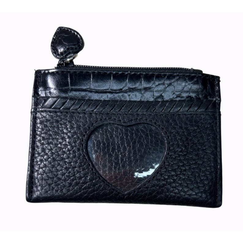 Puede incluir: Tarjetero de cuero negro con ventana en forma de coraz&oacute;n y cremallera en la parte superior. El tarjetero tiene una superficie texturizada y un tirador de cremallera en forma de coraz&oacute;n. Mide aproximadamente 10 cm de ancho y 7,6 cm de alto.