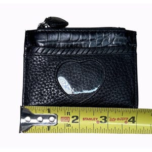 Puede incluir: Tarjetero de cuero negro con un recorte en forma de coraz&oacute;n y una cremallera en la parte superior. El tarjetero mide aproximadamente 10 cm de ancho. El dise&ntilde;o incluye un acabado de cuero texturizado y un ribete decorativo.
