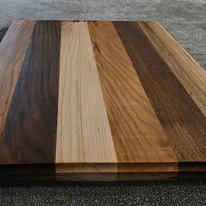 May include: A rectangular wooden chopping board with a natural finish. The board is made from multiple types of wood, including light and dark wood, creating a striped pattern.
