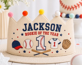 以下が含まれることがあります： JACKSON ROOKIE OF THE YEARという刺繍文字と数字の1が入ったベージュの布製クラウン。野球帽、野球ボール、ユニフォーム、グローブ、交差したバットの刺繍が施されています。上端はカラフルなポンポンで飾られています。