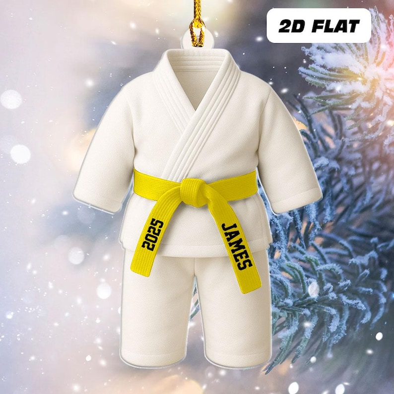 May include: A white karate uniform ornament with a yellow belt. The belt is personalized with the name "JAMES" and the year "2025". The ornament is labeled "2D FLAT".