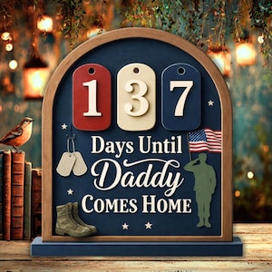 May include: Wooden countdown sign with the text "Days Until Daddy Comes Home." The sign features the numbers 137 on red, cream, and blue tags, along with an American flag and a soldier silhouette. Includes military dog tags and boots.