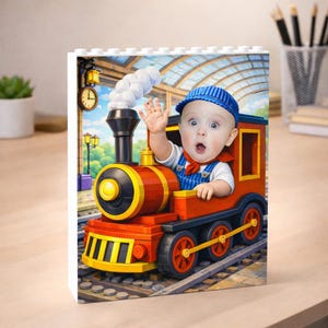 May include: A colorful block featuring a baby dressed as a train conductor waving from a toy train. The train is red and yellow, with black accents and a white smoke effect. The baby wears a blue striped cap and overalls.