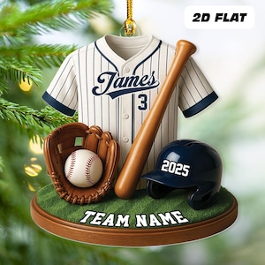 May include: Baseball-themed ornament featuring a jersey with "James 3", a baseball bat, a glove, a baseball, and a helmet with "2025". The ornament is on a green surface with "TEAM NAME" text.