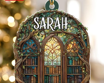 May include: A decorative ornament featuring a library scene with the name "SARAH" in white. The ornament has a stained-glass window design with bookshelves and is framed by tree branches and leaves. The ornament is labeled "2D FLAT".