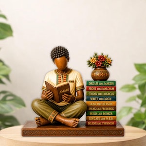 Puede incluir: Una figura de madera de una persona leyendo un libro titulado "AMARI", sentada sobre una base de madera. Junto a la figura hay una pila de libros con citas inspiradoras y un jarr&oacute;n de flores. La figura est&aacute; pintada en tonos tierra.