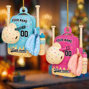 May include: Two baseball-themed ornaments. One is light blue, the other is pink. Each features a backpack design with a helmet, mitt, bat, and water bottle. The text "YOUR NAME", "00", and "Team name" are visible.