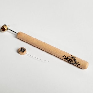 Puede incluir: Una herramienta de madera con un diseño geométrico, una pequeña perilla de madera con un diseño similar y un alambre delgado unido a la perilla.
