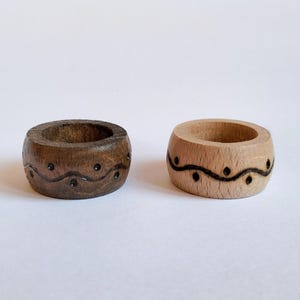 May include: Two wooden rings with a carved wavy design and black dots. The ring on the left is dark brown and the ring on the right is light brown.