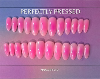 May include: Two sets of oval-shaped, pink press-on nails with a gradient effect. The nails transition from a lighter pink at the base to a brighter pink at the tips. The text "PERFECTLY PRESSED" and "NAILS BY C.C" are visible.