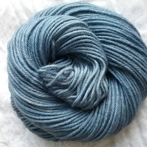 May include: A ball of blue yarn, tightly wound with visible strands. The yarn has a gradient effect, transitioning from a darker to a lighter shade of blue. The yarn is likely made of wool or a similar fiber, suitable for knitting or crocheting projects.