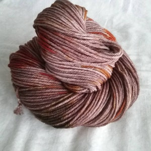 May include: A skein of yarn in shades of pink, brown, and orange. The yarn is twisted and has a mottled appearance.