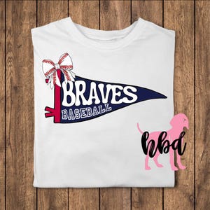 May include: White t-shirt with a blue and red pennant that says "Braves Baseball" and a red, white, and blue baseball-themed bow.