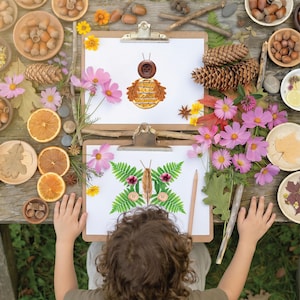 May include: Two clipboards with children's art of a bee and a butterfly, created with natural items like leaves and buttons. The artwork is surrounded by flowers, acorns, and dried oranges on a rustic wooden table, evoking a nature theme.