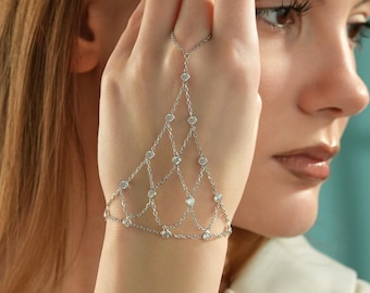 May include: A silver-toned hand chain featuring a delicate lattice design composed of thin metal links. The jewelry piece includes a ring component that connects to a bracelet section, adorned with small, clear, round-cut stones at each junction.